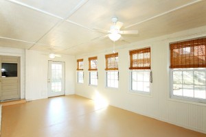 Large enclosed sunroom with a wall of windows and two doorways to the outside; freshly painted with two new ceiling fans